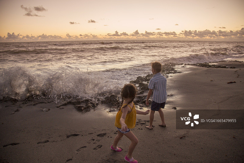 日出时分，男孩和姐姐在海滩上躲避海浪，地点：美国佛罗里达州朱庇特岛图片素材