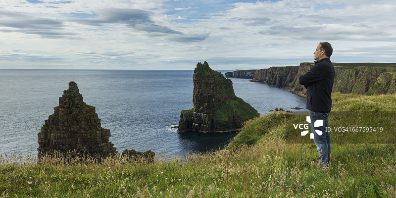 男人眺望北海，崎岖悬崖与海蚀柱图片素材