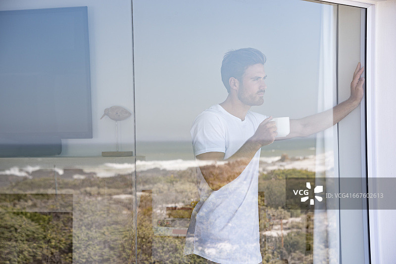 手持咖啡杯望向窗外的年轻男人图片素材