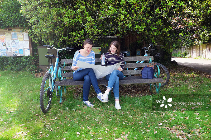 年轻姐妹和自行车坐在长凳上看地图图片素材