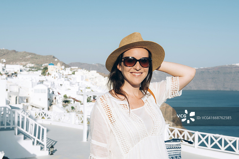 希腊圣托里尼伊亚：戴太阳镜和草帽的微笑女人肖像图片素材