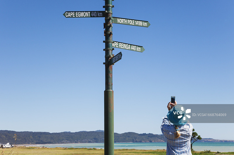 新西兰北岛东开普，女子在蒂阿拉罗瓦用手机拍摄路标图片素材