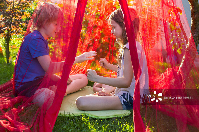 姐弟在蚊帐下的花园里玩石头剪刀布图片素材