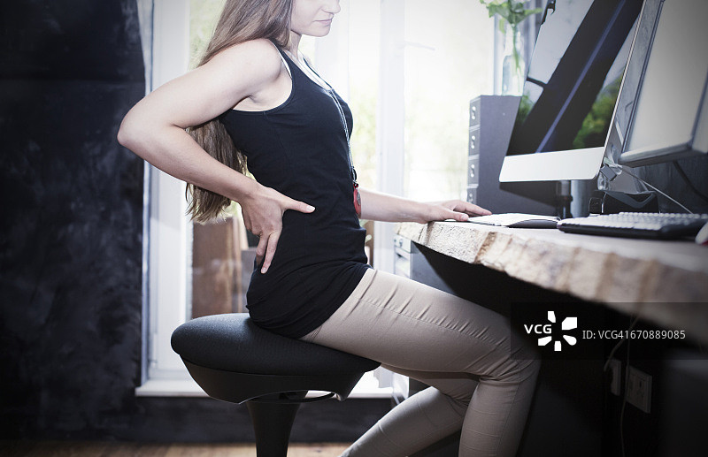 女人坐在办公桌旁的保健椅上，扶着后背图片素材