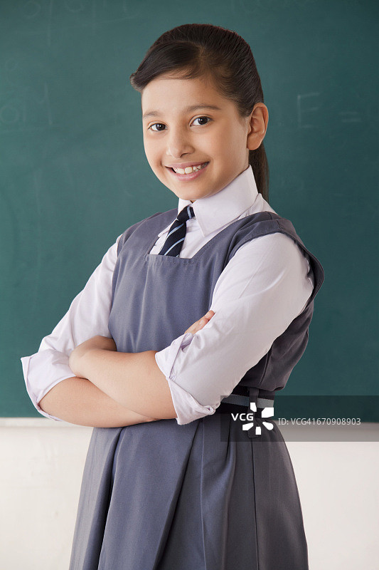 双臂交叉站在教室黑板前微笑女孩肖像图片素材