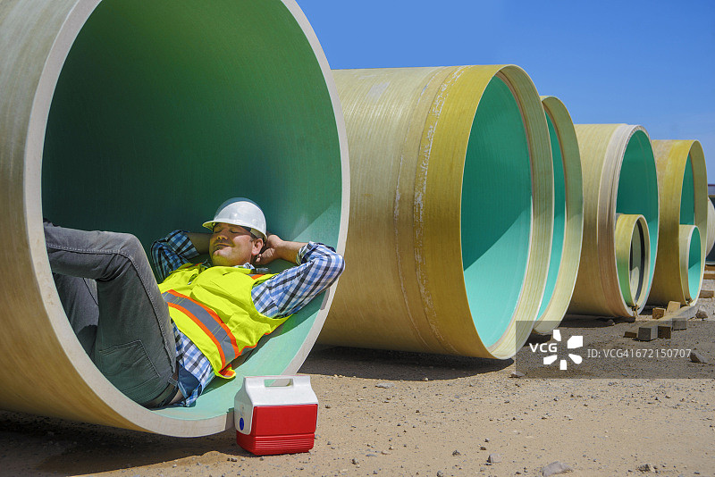 在大型管道内小憩的白人建筑工人图片素材