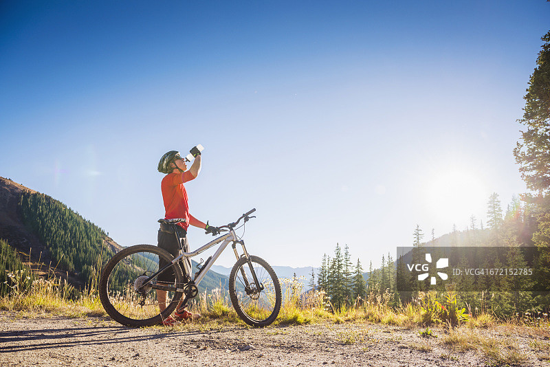 在山里骑山地自行车喝水的白人男子图片素材
