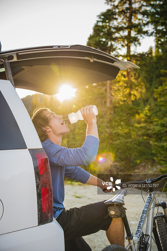 白人男子在汽车舱口喝水，旁边是山地自行车图片素材