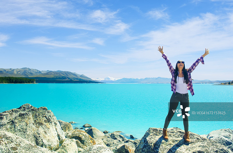 穿着格子衬衫在蓝色山湖庆祝的西班牙裔女人图片素材