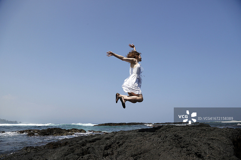 在海滩岩石上喜悦跳跃的女人图片素材