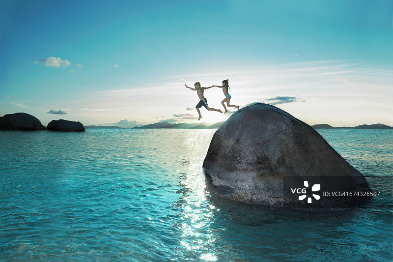 两个孩子手牵着手从岩石上跳入海中图片素材