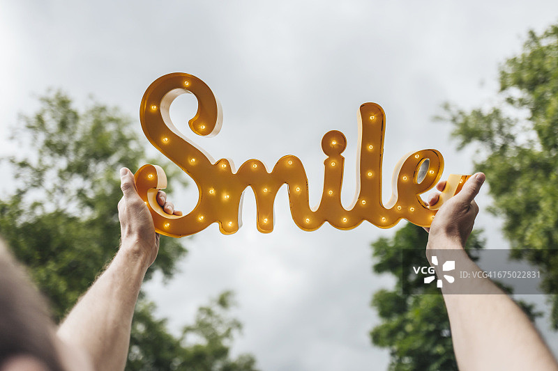 男人高举着闪闪发光的“微笑”字样图片素材