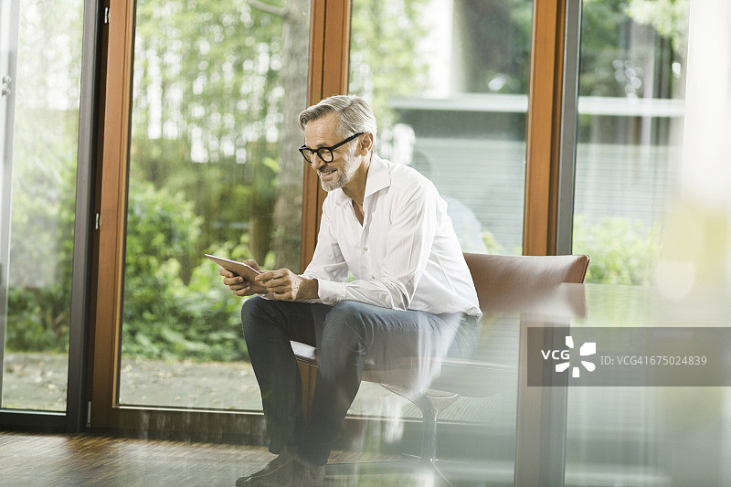 坐在客厅椅子上使用平板电脑的男人图片素材