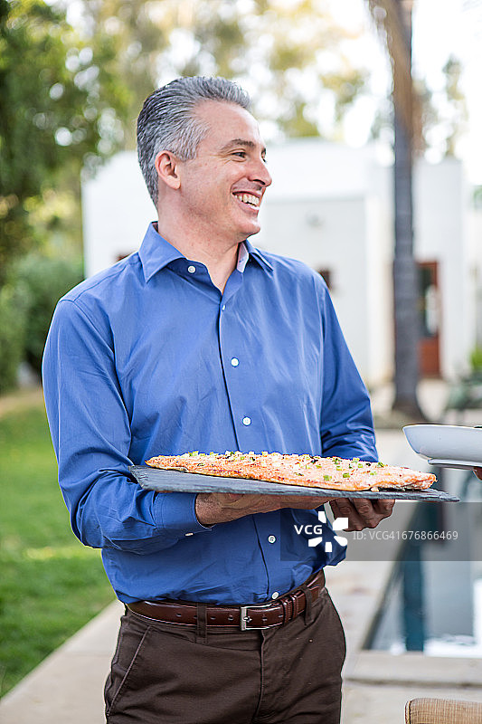 中年男人在花园聚会上手拿砧板上的鱼料理图片素材