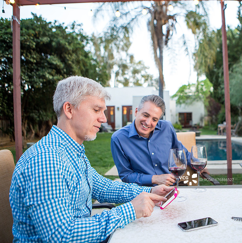 两位中年男人在花园派对的桌旁看智能手机图片素材