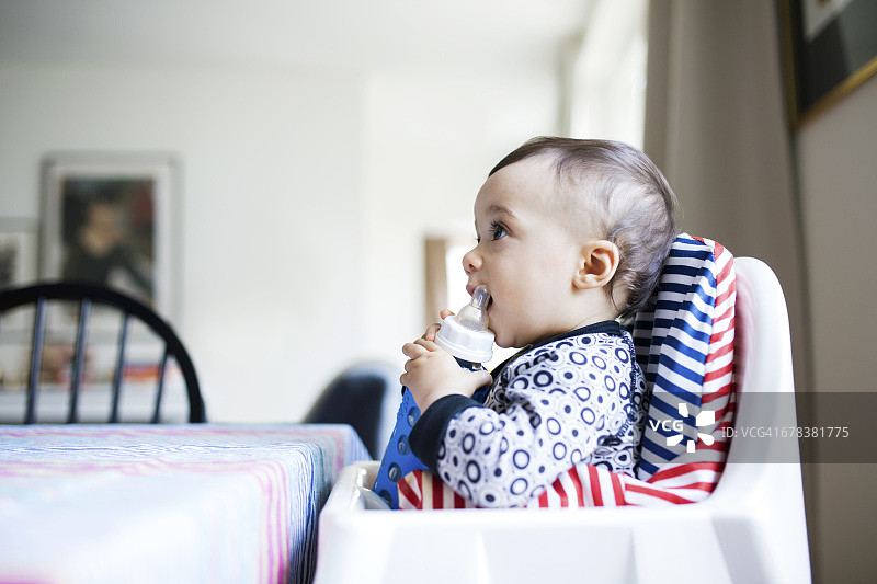 坐在高脚椅上喝奶瓶的女婴侧面照图片素材