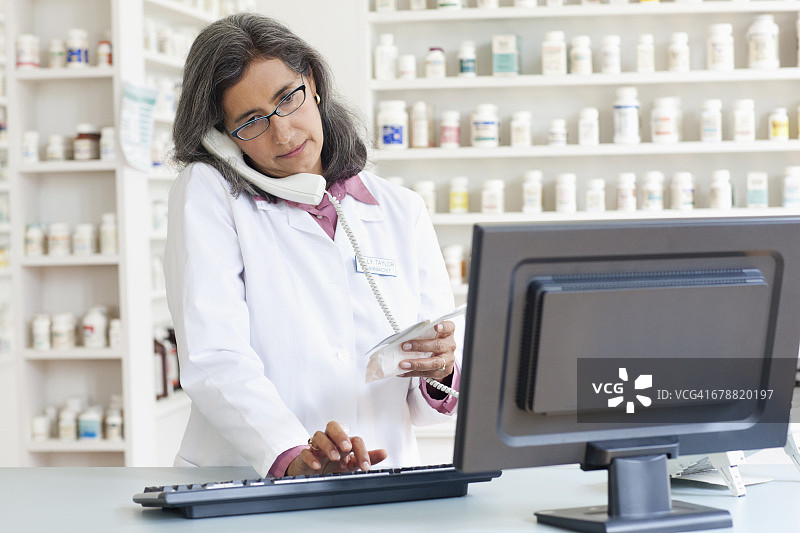 使用电脑并通过电话交谈的拉美裔药剂师图片素材