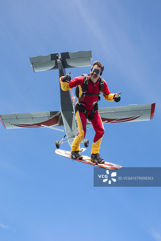 男子从飞机上跳下玩空中滑板，面带微笑图片素材