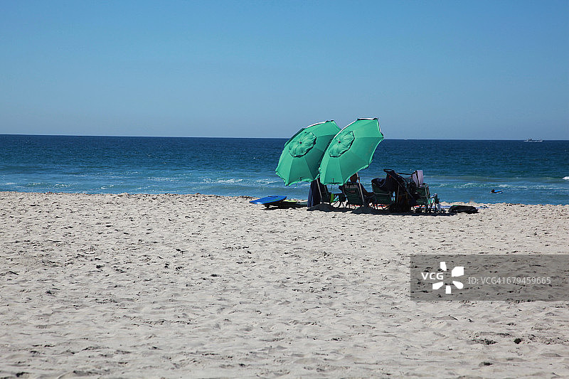 在海滩上撑着两把绿色雨伞的人们图片素材