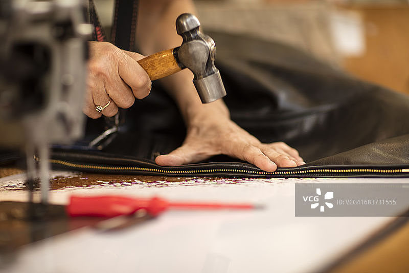 男人在皮夹克制造商中锤击夹克上的拉链特写图片素材