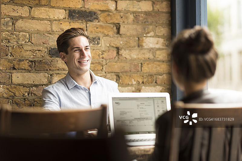 年轻商人和女人在咖啡馆使用笔记本电脑交谈图片素材