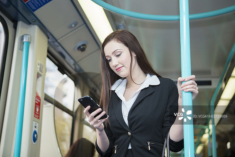 在伦敦码头区轻轨列车上使用手机的女商人图片素材