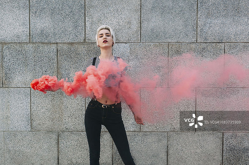 自信的年轻女子靠墙站立，手持遇险照明弹图片素材