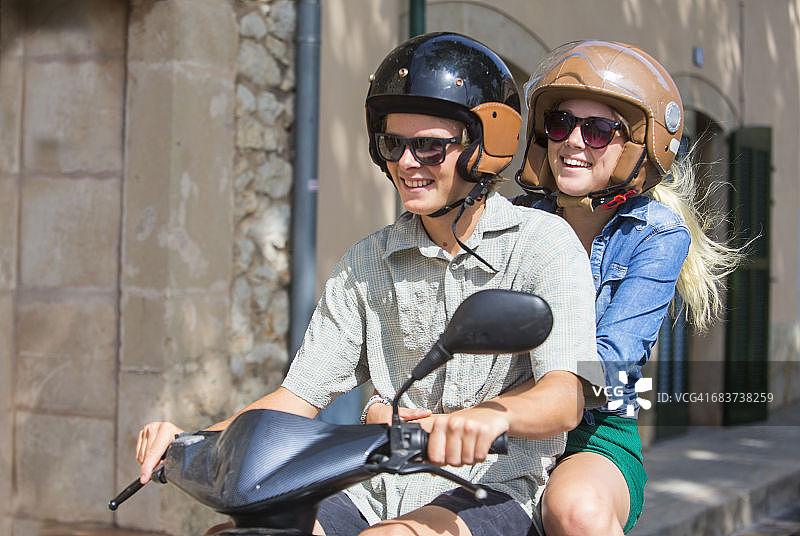 年轻夫妇骑着轻便摩托车穿过西班牙马略卡岛的村庄图片素材