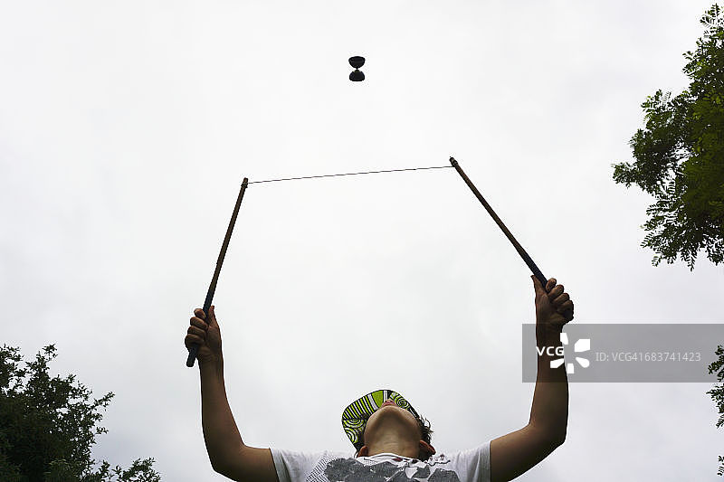 低角度拍摄：男孩在空中玩空竹图片素材