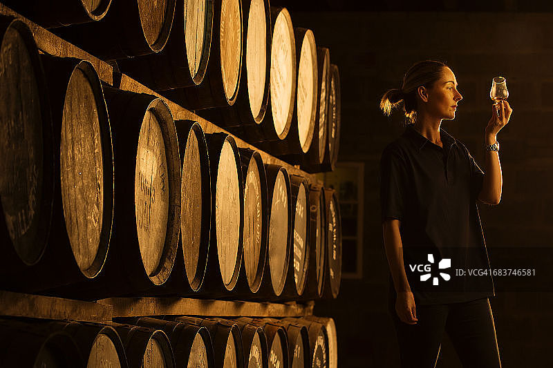 女品酒师在威士忌酒厂观察玻璃杯中威士忌的颜色图片素材