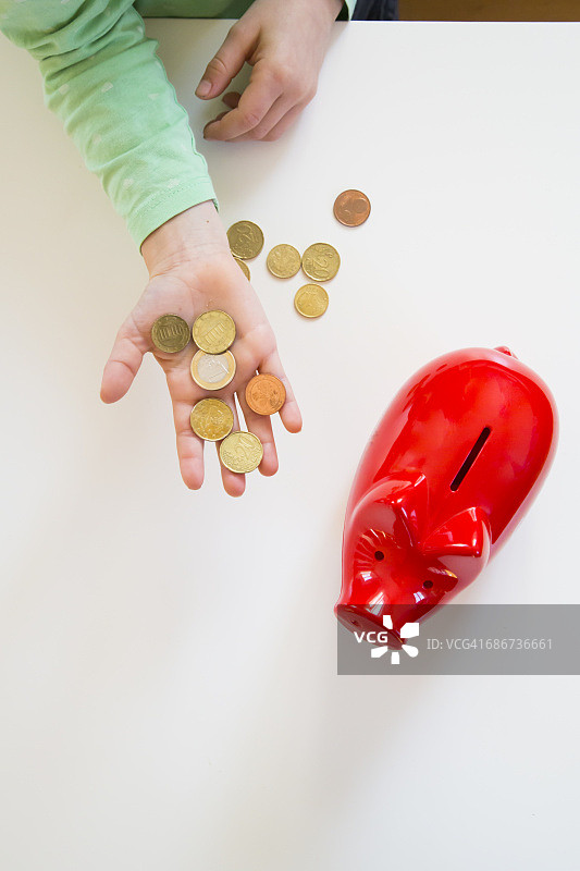女孩的手拿着硬币和一个红色小猪储蓄罐图片素材