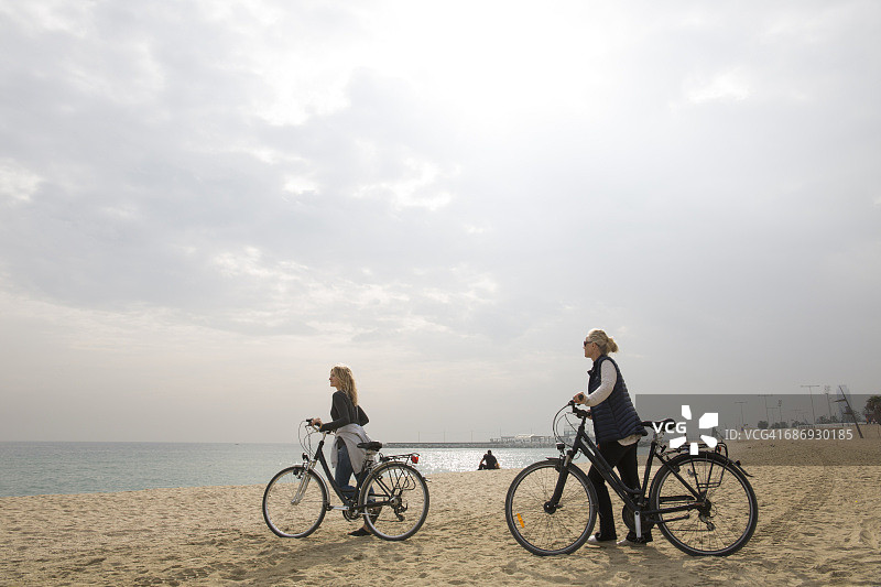 母亲和女儿在海滩上推着自行车图片素材