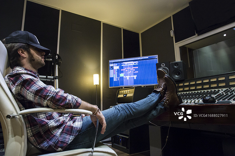 男人在录音棚里把脚放在调音台上休息图片素材