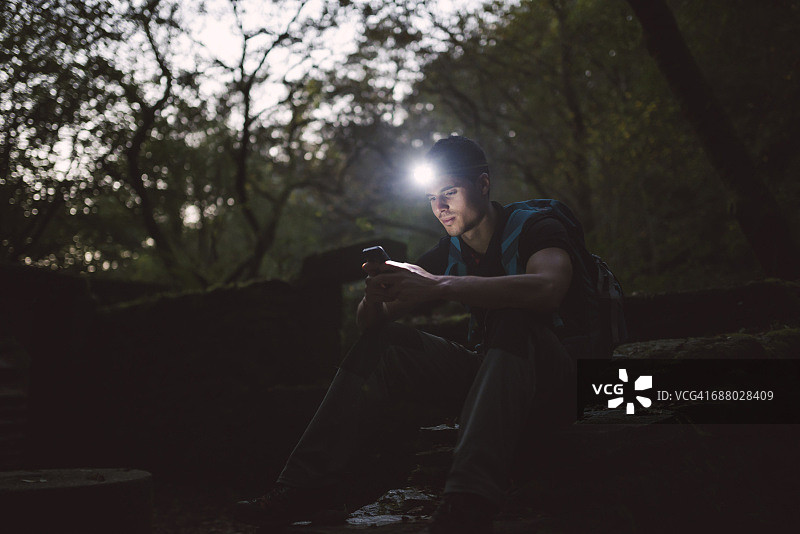 戴着头灯的徒步旅行者在森林里看手机图片素材