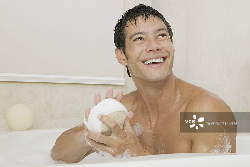 年轻男子在浴缸里拿着丝瓜瓤的特写图片素材