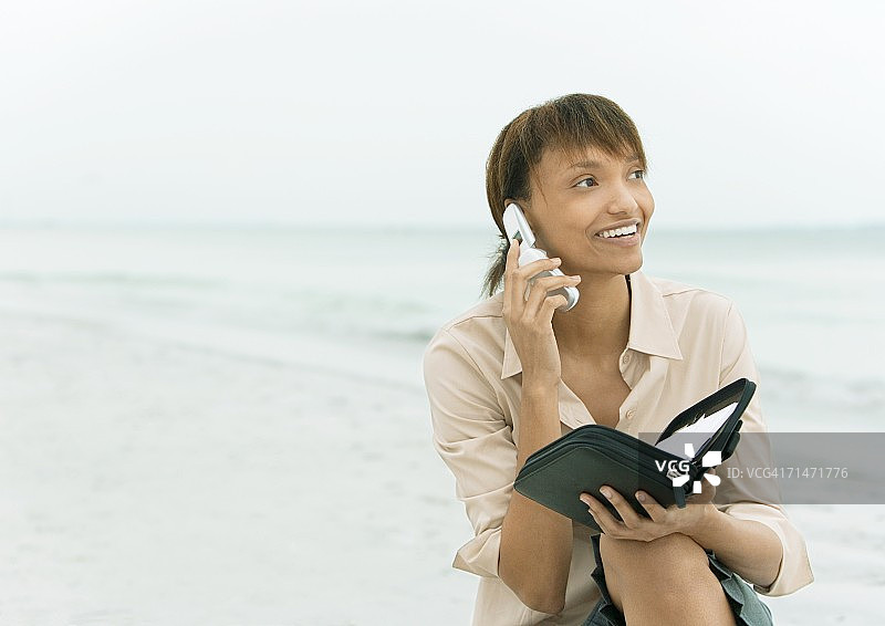 女人使用手机并拿着行程表，背景是海图片素材
