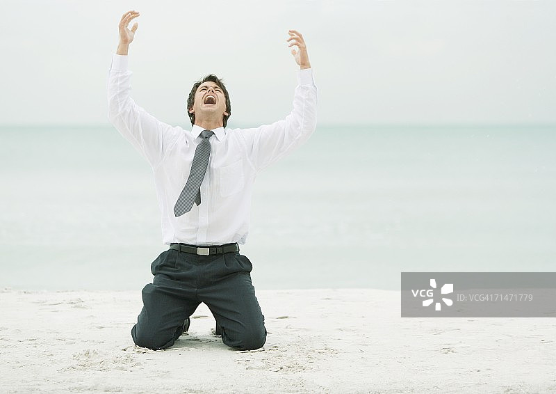 在海滩上跪着，张开双臂仰头的商人图片素材