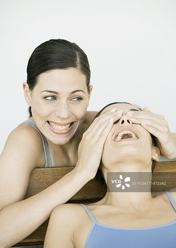 年轻女子遮住朋友的眼睛，两人都在微笑图片素材