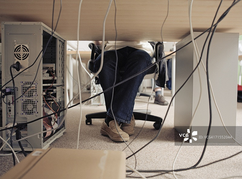 男子坐在桌旁，电脑后方插着电缆图片素材