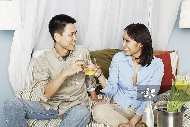 年轻夫妇坐在床上用酒杯敬酒图片素材