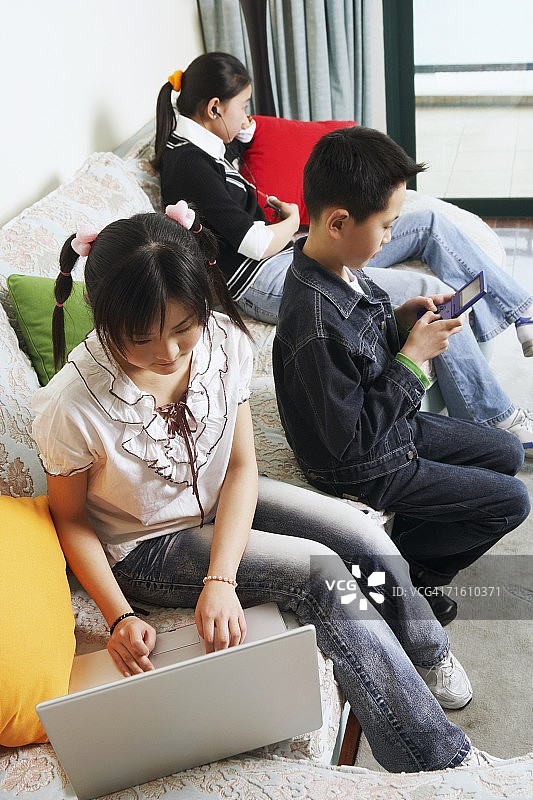 年轻女子和弟弟妹妹在沙发上用笔记本电脑的高角度视角图片素材