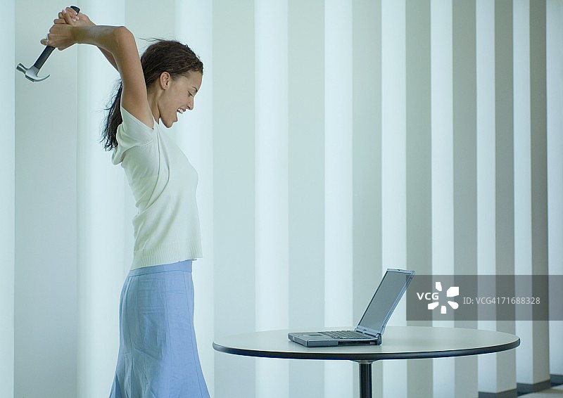 女人对着笔记本电脑大喊并挥舞锤子图片素材