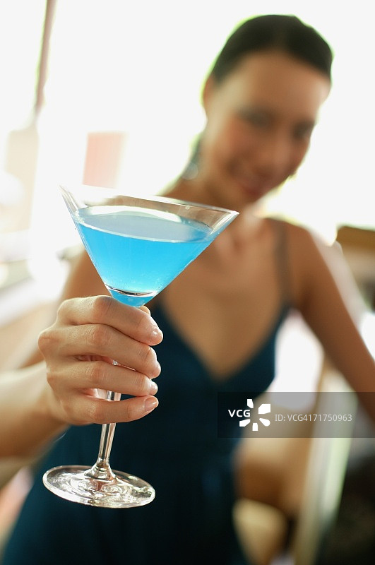 坐在吧台边手持鸡尾酒的女人，焦点选择图片素材