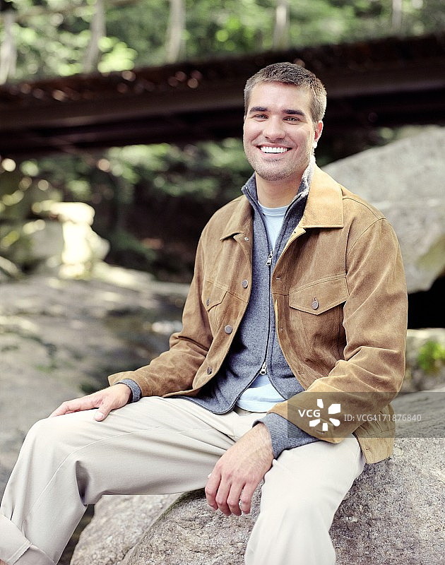 在纽约州新帕尔茨小溪边的岩石上微笑的年轻男人图片素材