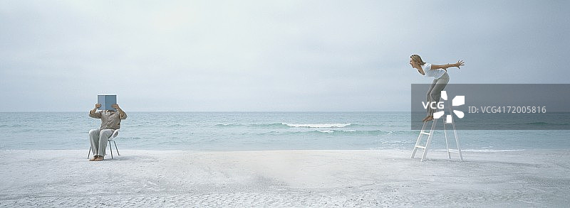 海滩上，男子举书遮面，女子在梯子上尖叫图片素材