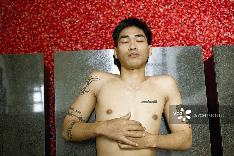 中年男人躺在满是玫瑰花瓣的热水浴缸旁边的地板上（高角度）图片素材