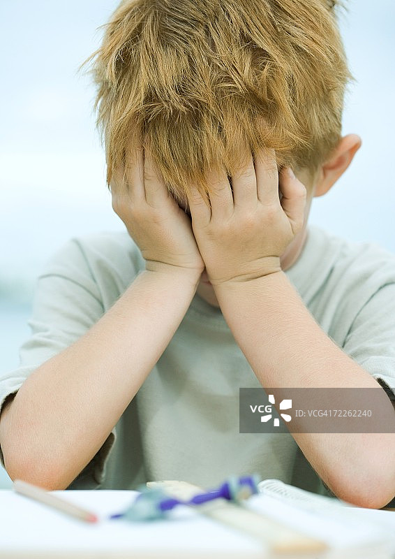 男孩捂着脸，面前的桌子上放着家庭作业图片素材