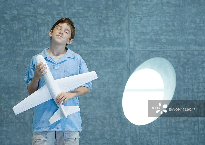 男孩手持玩具飞机，闭着眼睛图片素材