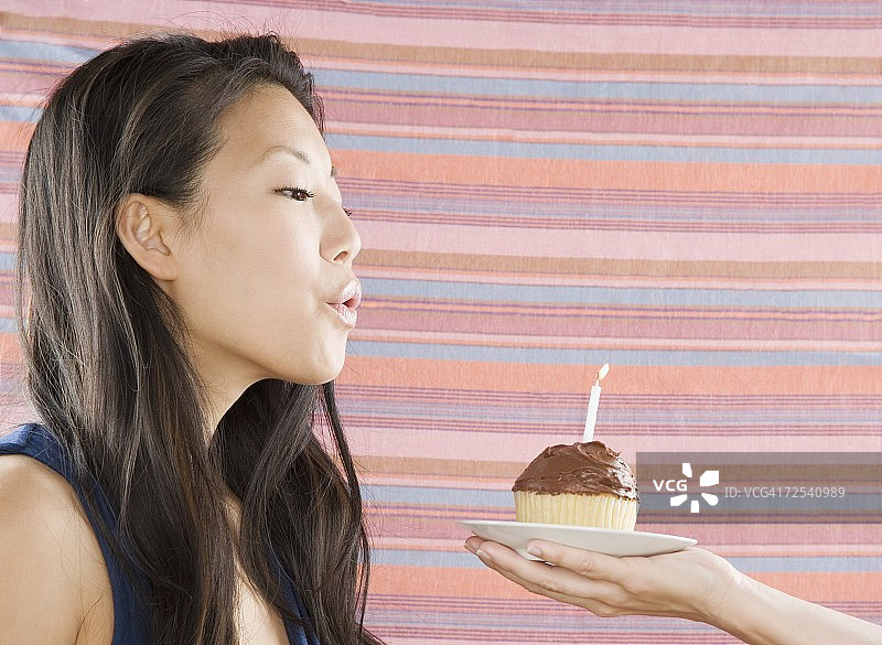 年轻的亚洲女性吹灭纸杯蛋糕上的蜡烛图片素材