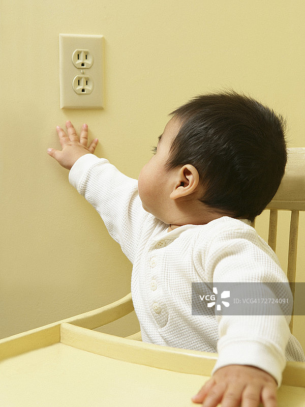 坐在高脚椅上伸手去够电源插座的男婴（15-18个月）图片素材